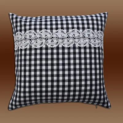 Ein quadratisches Kissen mit schwarz-weißem Karomuster und einem horizontalen Streifen dekorativer weißer Spitze in der Mitte vor einem Hintergrund mit braunem Farbverlauf.