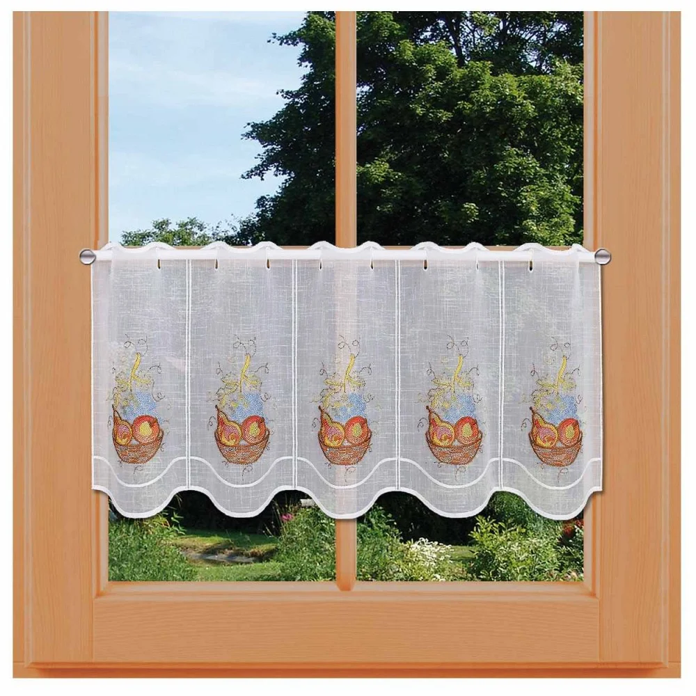 Ein Fenster, geschmückt mit einer kurzen, weißen Stickmuster-Scheibengardine mit bunten Stickereien von Obstkörben. Die Kollektion-Gardine hat eine gewellte Unterkante und lässt Licht herein, sodass draußen ein üppiger, grüner Garten mit Bäumen zu sehen ist. Die Gardine ist an einer hellen Holzstange aufgehängt.