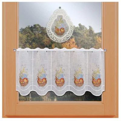 Ein Fensterrahmen aus Holz, an dessen oberem Ende ein weißes Fensterbild hängt, auf dem ein Obstkorb aufgestickt ist. Darunter verdeckt eine kurze weiße Stickmuster-Scheibengardine aus der Kollektion MT, ebenfalls mit einem Obstkorb-Motiv bestickt, das Fenster teilweise und gibt den Blick auf Bäume im Hintergrund frei.