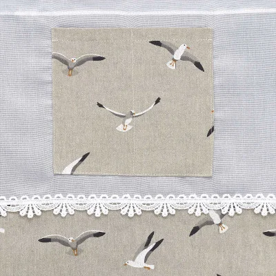 Ein neutraler Stoff zeigt eine quadratische Tasche mit einem aufgedruckten Muster von Möwen im Flug, das zum Hintergrund passt und die Tasche unauffällig macht. Unterhalb der Tasche befindet sich eine weiße Spitzenborte, die ein zusätzliches dekoratives Detail darstellt.
