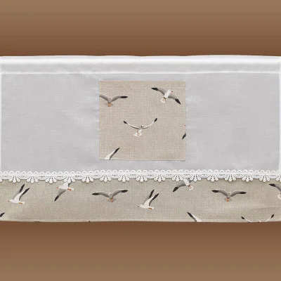 Ein weißer Scheibenhänger mit Spitzenbesatz und einer beigen Platte am unteren Rand, die jeweils ein fliegendes Möwenmuster zeigen. Ein kleiner quadratischer Aufnäher mit demselben Möwenmuster befindet sich in der Mitte über der Spitzenbordüre. Der Hintergrund ist braun.