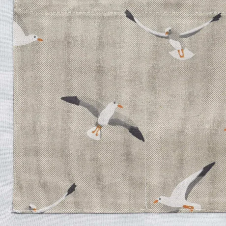 Beigefarbener Stoff mit einem sich wiederholenden Muster aus weißen Möwen in verschiedenen Flugpositionen. Die Möwen haben orangefarbene Schnäbel und Füße mit schwarz bestückten Flügeln. Die Textur des Stoffes ist sichtbar, und am linken Rand befindet sich ein weißer Stoff.