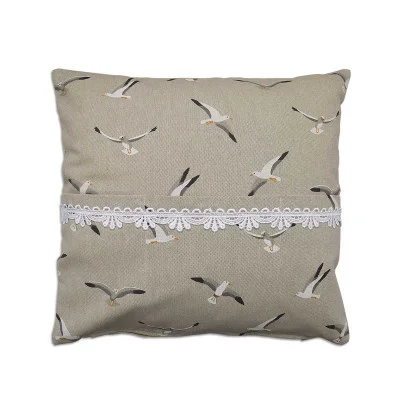 Ein quadratisches beiges Kissen (40 x 40 cm) mit einem Muster aus Möwen in verschiedenen Flugposen. Eine weiße dekorative Spitzenbordüre verläuft horizontal über die Mitte des Kissens. Der Hintergrund ist einfarbig und hebt die Vogelillustrationen und die Spitzenverzierung hervor.