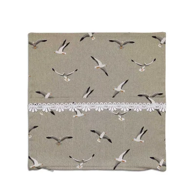 Eine quadratische, beigefarbene Kissenhülle mit aufgedruckten Abbildungen von Möwen in verschiedenen Flugpositionen auf einfarbigem Hintergrund und einem horizontalen Streifen weißer Spitze in der Mitte.