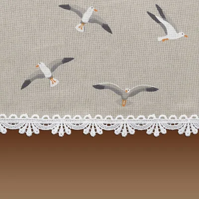 Der beigefarbene Stoff zeigt Illustrationen von vier Möwen im Flug, die über einer weißen gehäkelten Spitzenborte am unteren Rand positioniert sind. Unterhalb der Spitze geht der Hintergrund in einen braunen Farbverlauf über.