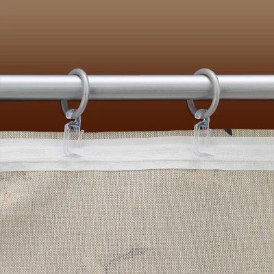 Nahaufnahme eines beigen Stoffvorhangs, der an einer silbernen Vorhangstange aufgehängt und mit transparenten Kunststoffhaken und runden Silberringen befestigt ist. Der Hintergrund hat einen braunen Farbverlauf.