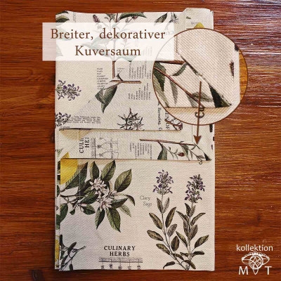 Ein gefalteter Tischläufer mit Blumen- und Kräutermotiven auf einer Holzoberfläche mit einer Nahaufnahme, die detaillierte botanische Illustrationen und Text zeigt. Die Tischdecke hat einen breiten Kuvertsaum und einen Pfeil, der auf den Saum zeigt.