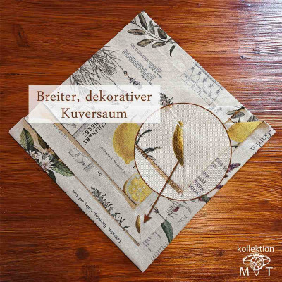 Eine gefaltete Tischdecke mit Blumen- und Kräutermotiven auf einer Holzoberfläche mit einer Nahaufnahme, die detaillierte botanische Illustrationen und Text zeigt. Die Mitteldecke hat einen breiten Kuvertsaum und einen Pfeil, der auf den Saum zeigt.