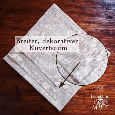 Gefaltete beige Tischdecke mit Blumenmuster auf einem Holztisch. Eine Lupe hebt den breiten, dekorativen Saum mit der Aufschrift „Breiter, dekorativer Kuvertsaum“ hervor. In der unteren rechten Ecke steht der Text „kollektion MT“.