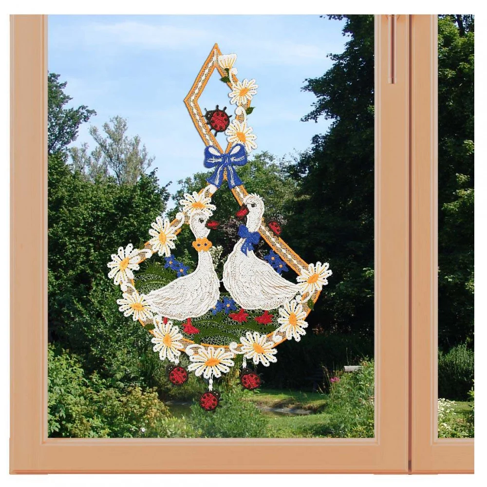 Ein bezauberndes Fensterbild zeigt exquisite Vogtländische Spitze mit zwei weißen Enten inmitten von Blumen, Beeren und einer blauen Schleife. Es hängt anmutig an einem hellen Holzfenster und rahmt die idyllische Landhaus-Idylle mit grünen Bäumen und Sträuchern dahinter ein.