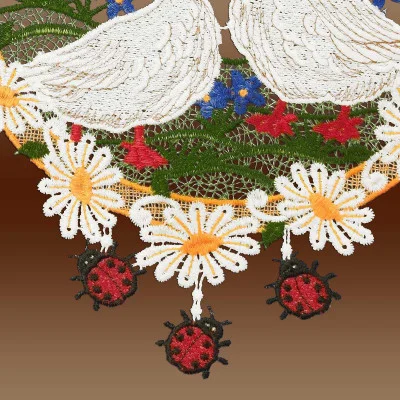 Aufwendige Spitzenstickerei im Stil der Vogtländischen Spitze zeigt zwei weiße Gänse über einem Kranz aus weißen Gänseblümchen und roten Marienkäfern. Grünes Gras und blaue Blumen vervollständigen dieses harmonische Fensterbild und erinnern an eine heitere Landhaus-Idylle.