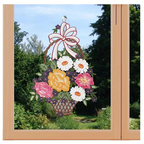 Ein Korb mit leuchtenden, gestickten Blumen in Rosa, Orange und Weiß hängt wie ein bezauberndes Fensterbild am Fenster. Mit einer großen Schleife verziert, harmoniert er perfekt mit den üppigen grünen Bäumen draußen.