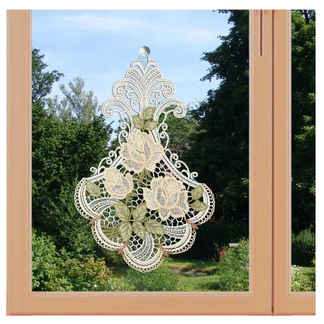 Ein dekoratives Ornament aus Vogtländischer Spitze mit komplizierten Blumenmustern hängt an einem Glasfenster vor dem Hintergrund eines üppig grünen Gartens.