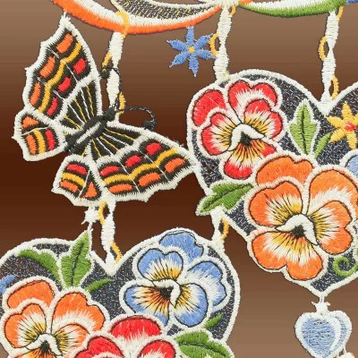 Eine Nahaufnahme leuchtender Stickereien, die an die Vogtländische Spitze erinnern. Sie zeigen einen Schmetterling mit roten und orangefarbenen Flügeln und farbenfrohe Blumen auf braunem Hintergrund. Die Blüten in Rot-, Orange- und Blautönen mit grünen Blättern erinnern an den Charme von Frühlingsherzen.