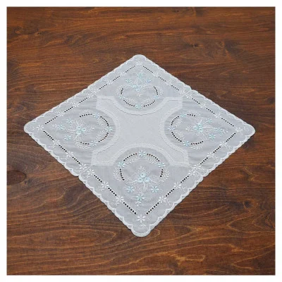 Ein weißes, quadratisches Baumwollbatist-Deckchen mit blauer Blumenstickerei und durchbrochenen Vogtländischen Spitzendetails liegt auf einer dunklen Holzoberfläche und bildet eine bezaubernde Tischdekoration.