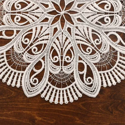 Naturfarbenes Spitzendeckchen, inspiriert von der Vogtländischen Spitze, mit einem filigranen, symmetrischen Muster auf einer dunklen Holzoberfläche. Dieses runde Deckchen eignet sich perfekt als Tischdekoration und besticht durch Wirbel, Schleifen und zarte Stickereien.