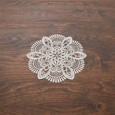 Ein weißes, aufwendig gemustertes, rundes Deckchen aus vogtländischer Spitze und einem Blumendesign ist auf einer dunkelbraunen Holzoberfläche zentriert und bildet eine elegante Tischdekoration.