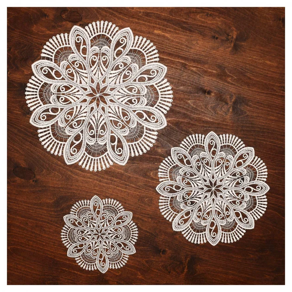 Drei kunstvoll gemusterte, runde weiße Deckchen aus Vogtländischer Spitze sind auf einer dunklen Holzoberfläche angeordnet. Die Deckchen zeigen florale und geometrische Muster und schaffen so eine dekorative und elegante Tischdekoration.
