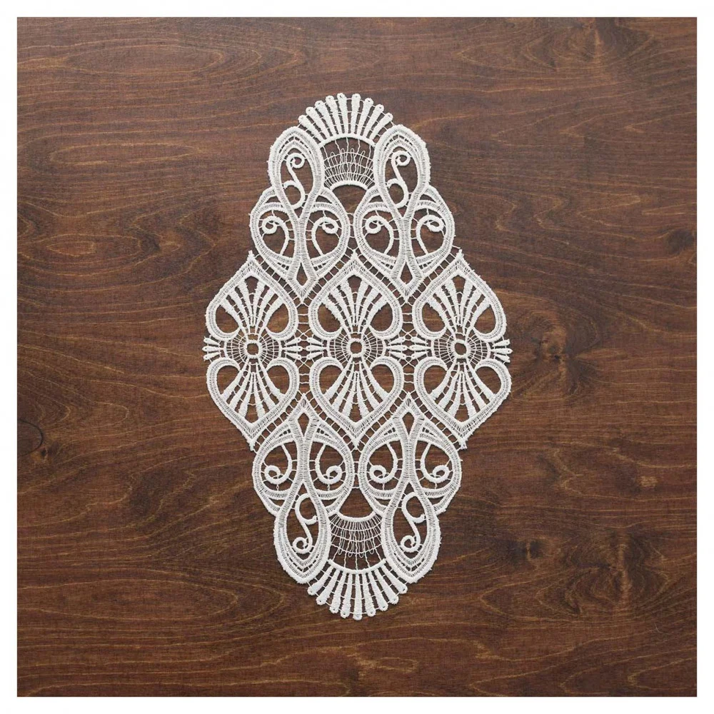 Ein naturfarbenes, aufwendig gemustertes Deckchen Amara aus Vogtländischer Spitze weist symmetrische, wirbelnde Designs auf und ruht elegant auf einer dunklen Holzoberfläche – eine raffinierte Tischdekoration.