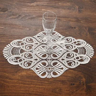 Zwei klare Sektgläser auf einem kunstvollen vogtländischen Spitzendeckchen Amara, beides auf einem dunklen Holztisch arrangiert, schafft eine raffinierte Tischdekoration.