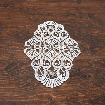 Ein naturfarbenes, aufwendig gemustertes Deckchen Amara aus Vogtländischer Spitze weist symmetrische, wirbelnde Designs auf und ruht elegant auf einer dunklen Holzoberfläche – eine raffinierte Tischdekoration.