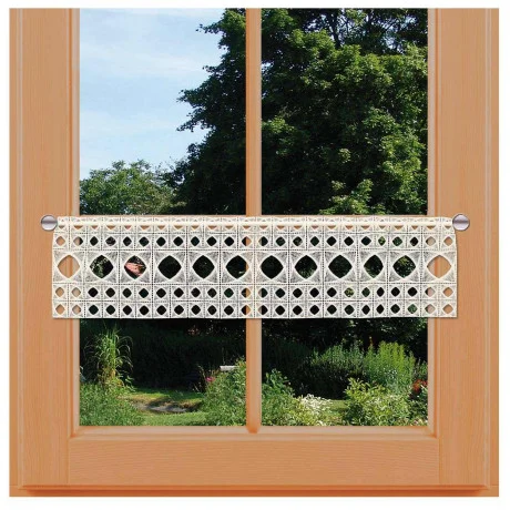 Ein Fenster mit Holzrahmen und einem dekorativen, gestickten Spitzenpaneel im unteren Teil; draußen sind üppige grüne Bäume und Gartenpflanzen unter einem strahlenden Himmel sichtbar.