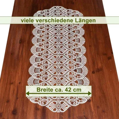 Auf einem Holztisch liegt der dekorative Tischläufer Amara aus vogtländischer Spitze mit aufwendigem Muster. Der Text oben lautet „viele verschiedene Längen“ und unten „Breite ca. 42 cm“, perfekt für elegante Tischdekoration.