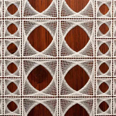 Weiße Spitzenkunst, die geometrische quadratische und kreisförmige Muster bildet, ist in einem Raster auf einem hölzernen Hintergrund angeordnet, wodurch ein dekoratives und kompliziertes Design mit überlappenden Linien und offenen Flächen entsteht.