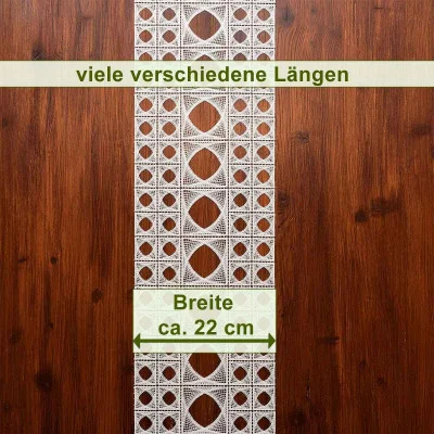 Ein Tischläufer aus weißer Spitze mit geometrischen Mustern liegt auf einer dunklen Holzoberfläche. Der Text auf Deutsch lautet „viele verschiedene Längen“ und „Breite ca. 22 cm“, wobei Pfeile die Breite angeben.