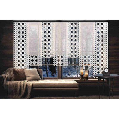 Ein gemütliches Wohnzimmer mit einem beigen Sofa und einer Decke liegt gegenüber einem großen Fenster, das mit der Flächengardine Miray und weißen, geometrisch gemusterten Vorhängen behangen ist. Draußen sind schneebedeckte Bäume zu sehen. Kerzen und eine Uhr stehen auf dem Fensterbrett.