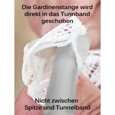 Eine Hand führt eine Gardinenstange in das Tunnelband einer Flächengardine Miray aus Vogtländischer Spitze in Ecru ein. Der deutsche Text erklärt, dass die Stange in das Tunnelband und nicht zwischen Spitze und Band eingeschoben werden soll.