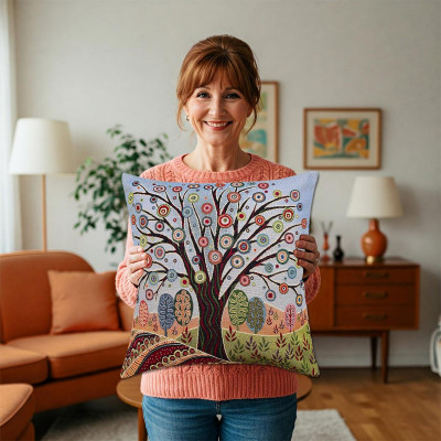 Eine lächelnde Frau in einem gemütlichen Wohnzimmer hält ein Gobelin-Dekokissen mit einem farbenfrohen, skurrilen Baummotiv mit komplizierten Mustern und leuchtenden Blättern in der Hand. Im Hintergrund sind Möbel und Kunstwerke aus der Mitte des Jahrhunderts zu sehen.