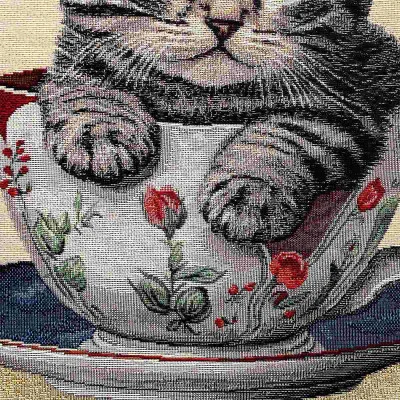 Ein grau getigertes Kätzchen sitzt gemütlich in einer mit Blumenmustern verzierten Teetasse und ruht mit seinen Vorderpfoten auf dem Rand; die Tasse steht auf einer passenden Untertasse.