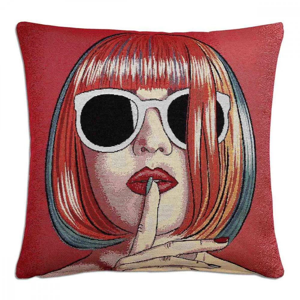 Ein dekoratives Kissen mit der Abbildung einer Frau mit rotem Bob-Haarschnitt, die eine große weiße Sonnenbrille und roten Lippenstift trägt und ihren Finger in einer „Pst“-Geste auf ihre Lippen legt, auf rotem Hintergrund.