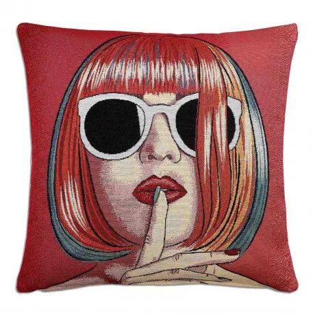 Ein dekoratives Kissen mit der Abbildung einer Frau mit rotem Bob-Haarschnitt, die eine große weiße Sonnenbrille und roten Lippenstift trägt und ihren Finger in einer „Pst“-Geste auf ihre Lippen legt, auf rotem Hintergrund.