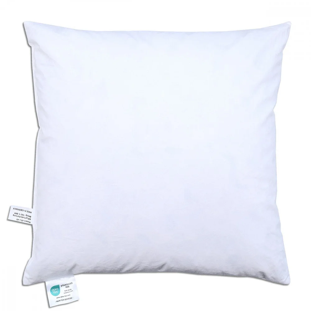 Ein schlichtes weißes quadratisches Kissen mit zwei Stoffanhängern an den unteren Ecken, vor einem weißen Hintergrund.