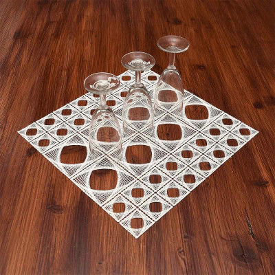 Vier umgedrehte Dektgläser sind auf einer weißen, geometrisch gemusterten Deckchen angeordnet, das diagonal auf einem Holztisch liegt.