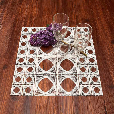 Ein brauner Holztisch mit einer weißen Tischdecke aus Spitze mit geometrischem Muster, auf dem zwei klare Gläser und ein Tafelaufsatz aus violetten und weißen Fliederblüten stehen.