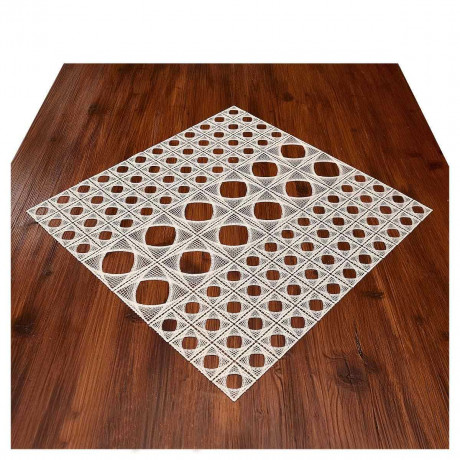 Eine gitterartige, geometrische Mitteldecke mit quadratischen und rautenförmigen Ausschnitten ist auf einem polierten Holztisch platziert, wodurch ein auffälliger Musterkontrast zwischen dem weißen Kunstwerk und dem dunklen Holz entsteht.