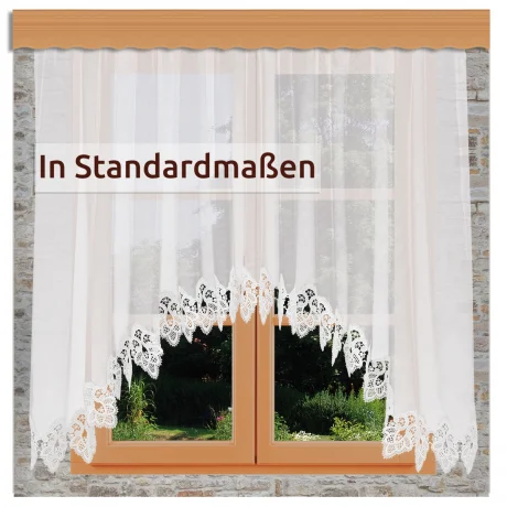 Ein Fenster mit durchsichtigen weißen Spitzenvorhängen. Der Text auf dem Bild lautet "In Standardmaßen". Aus dem Fenster blickt man auf einen grünen Garten mit Gras und Bäumen.