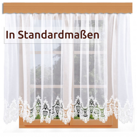 Weiße Spitzenvorhänge mit einem verschnörkelten Blumenmuster hängen an einer Holzstange vor einem Fenster. Ein Etikett mit den Worten "In Standardmaßen" befindet sich oben links auf dem Bild.