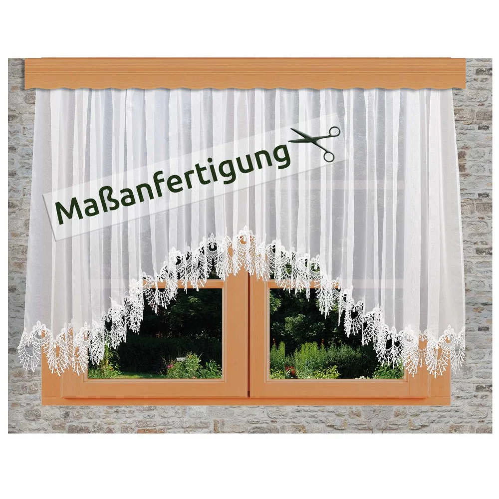 Weißer Spitzenvorhang mit floralen Mustern, der an einem Holzfenster in einer Steinwand hängt. Ein Schild mit Scherensymbol und dem deutschen Text "Maßanfertigung" ist über den Vorhang gelegt.