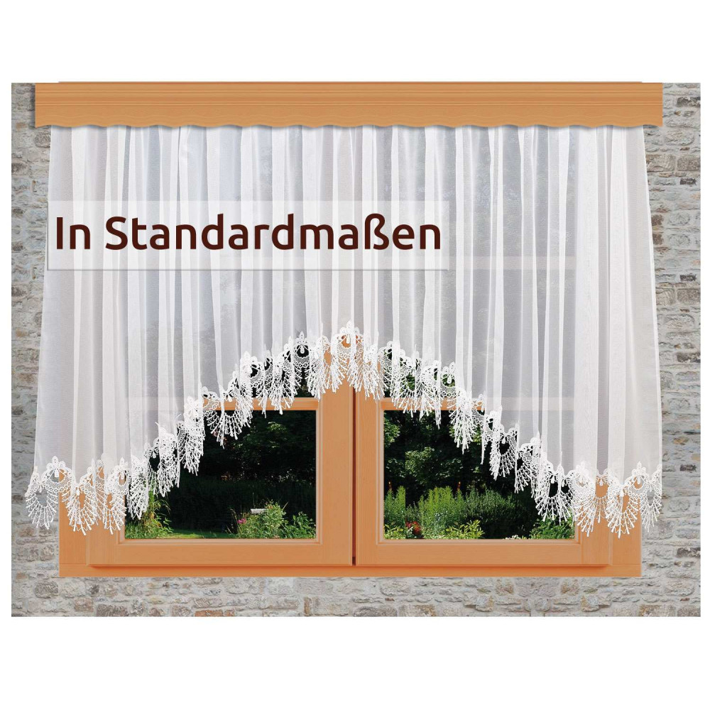 Ein Fenster mit durchsichtigen weißen Spitzenvorhängen, die eine florale Kante aufweisen. Draußen sind grünes Gras und Pflanzen zu sehen. Der Text auf dem Vorhang lautet: "In Standardmaßen.