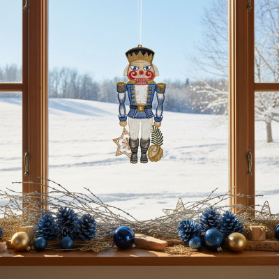 Ein Fensterbild Nussknacker Ornament hängt in einem Fenster mit Blick auf eine verschneite Landschaft. Die Fensterbank ist mit blauer und goldener Weihnachtsdekoration - Tannenzapfen, Ornamenten und Zweigen - geschmückt, während helles Sonnenlicht die festliche Szene beleuchtet.