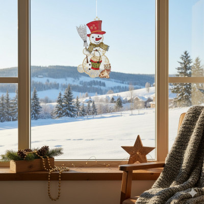 Ein gemütliches Zimmer mit einem Stuhl und einer Decke am Fenster bietet einen Blick auf eine verschneite Landschaft. An der Glasscheibe hängt ein Fensterbild Schneemann, während ein Stern, eine Tannengirlande und Holzperlen die Fensterbank mit einer charmanten Winterdekoration schmücken.