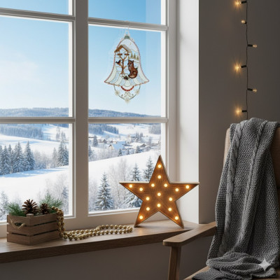 Eine gemütliche Winterszene am Fenster mit einer Schachtel, Plauener Spitze, einem Tannenzapfen, einer brennenden Sternlampe, einer grauen Strickdecke auf einem Stuhl, einer goldenen Perlengirlande und einer verschneiten Landschaft mit Bäumen und Häusern draußen.
