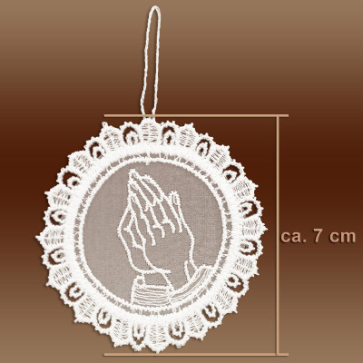 Ein kreisförmiges weißes Spitzenornament aus Plauener Spitze mit betenden Händen in der Mitte, Spitzenbordüren und einer Aufhängeschlaufe. Perfekt als Adventsbaumbehang, er misst ca. 7 cm im Durchmesser. Der Hintergrund ist braun.