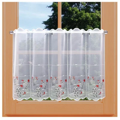 Ein Fenster mit heller Holzverkleidung wird von einem durchsichtigen weißen Vorhang verdeckt, auf dem gestickte Hühner mit roten Kämmen und kleinen roten Blumen zu sehen sind. Außerhalb des Fensters sind grüne Bäume und ein blauer Himmel zu sehen.