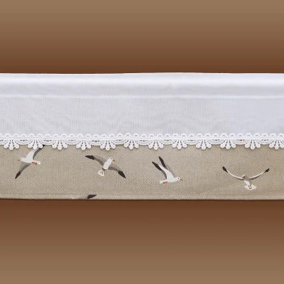 Eine Spitzengardine mit einem weißen oberen Rand, der mit weißer Spitze eingefasst ist, und einem beigen unteren Teil, der mit Abbildungen von fliegenden Möwen verziert ist. Der Hintergrund geht in einem sanften Farbverlauf von Beige zu Braun über. Höhe 20 cm