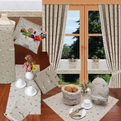 Eine Collage zeigt beigefarbene Stoffgegenstände mit einem Vogelmotiv: Vorhänge an einem Fenster mit Blick ins Grüne, eine Tischdecke, Tischsets, Kissen, einen Brotkorb, ein Teeservice und eine Blumenvase. Alle Gegenstände sind auf einem Holzboden und einem Tisch angeordnet.